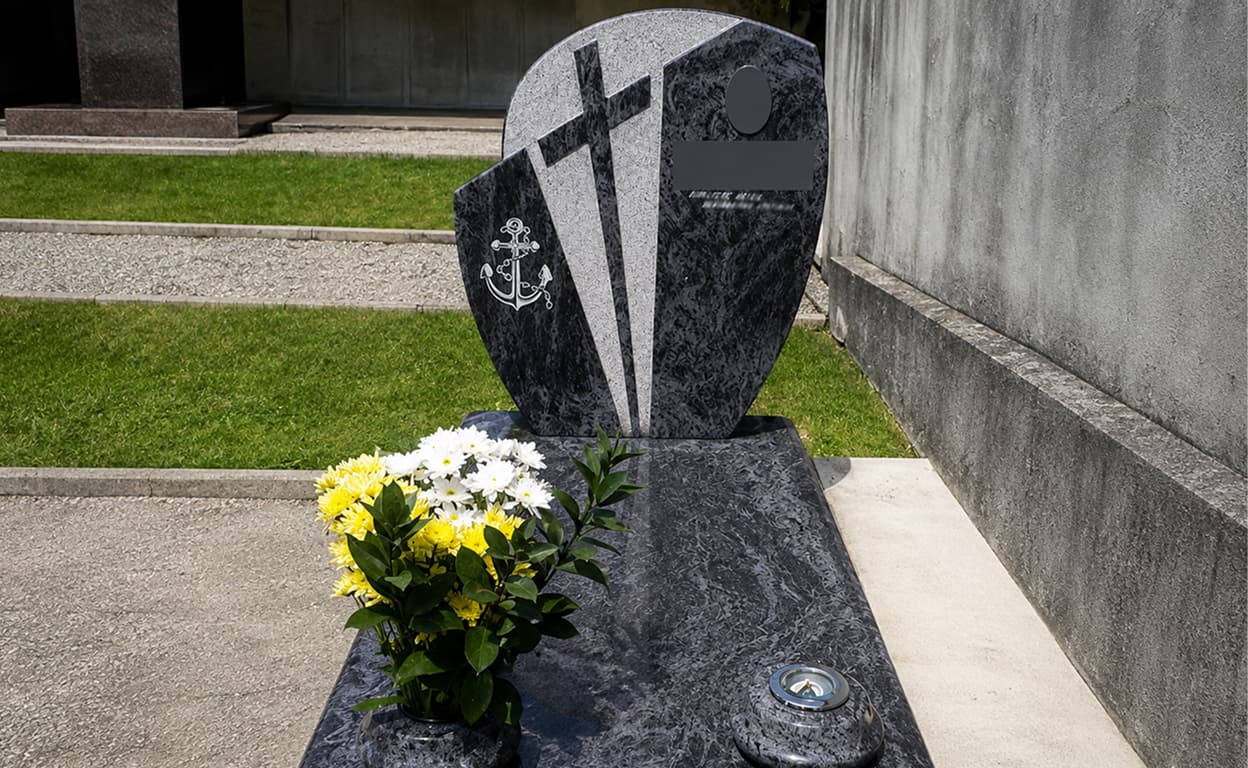Lapide nera lucida in granito con incisione a croce e ancore, fiori bianchi e gialli davanti, in un memoriale su pavimento e pareti in cemento grigio