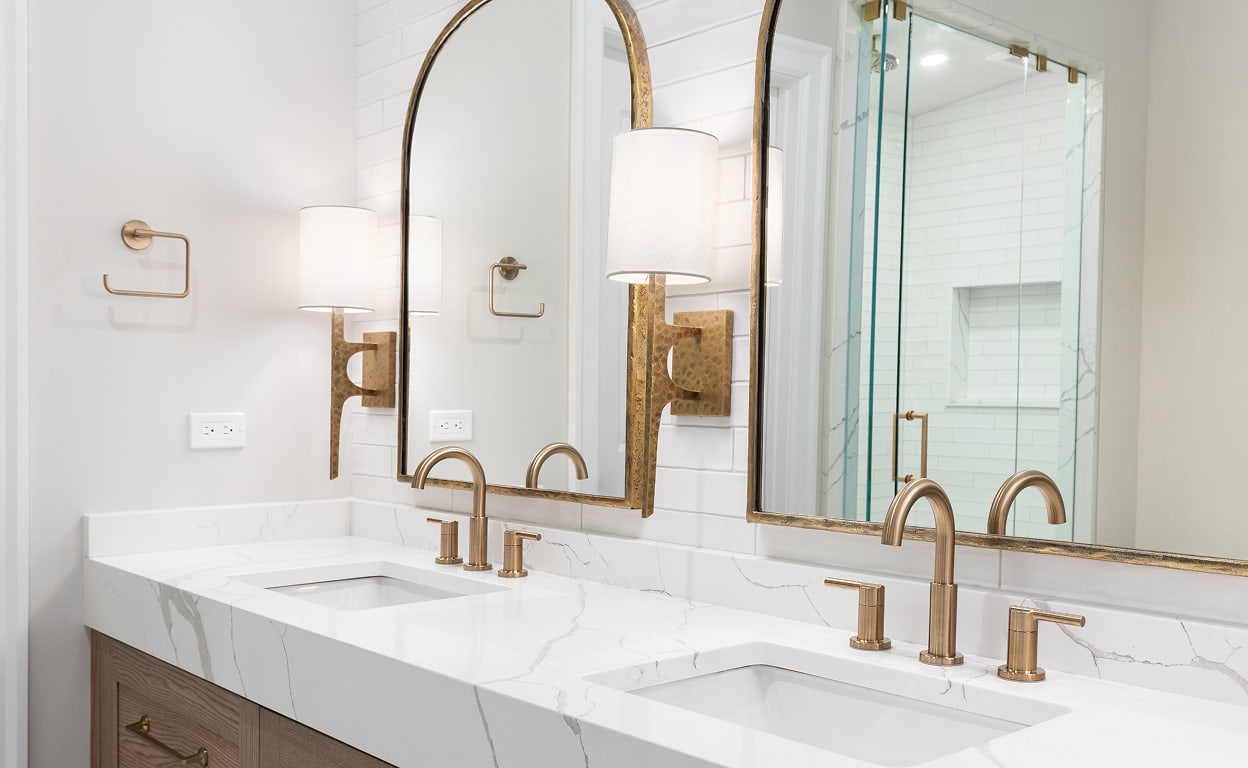 Bagno moderno con doppio lavabo in marmo bianco, rubinetteria dorata, specchio grande con cornice metallica e doccia in vetro trasparente, design elegante