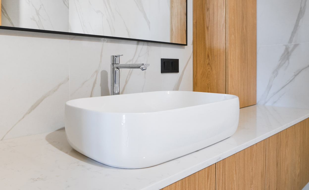 Lavabo da appoggio bianco in bagno moderno con piano in pietra e rubinetteria cromata, pareti chiare e inserti in legno