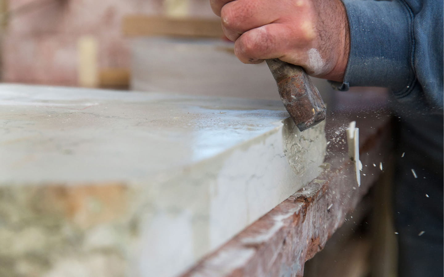 Falegname al lavoro con scalpello e martello, mentre taglia e scava una tavola di legno, con trucioli e polvere sul piano da lavoro.