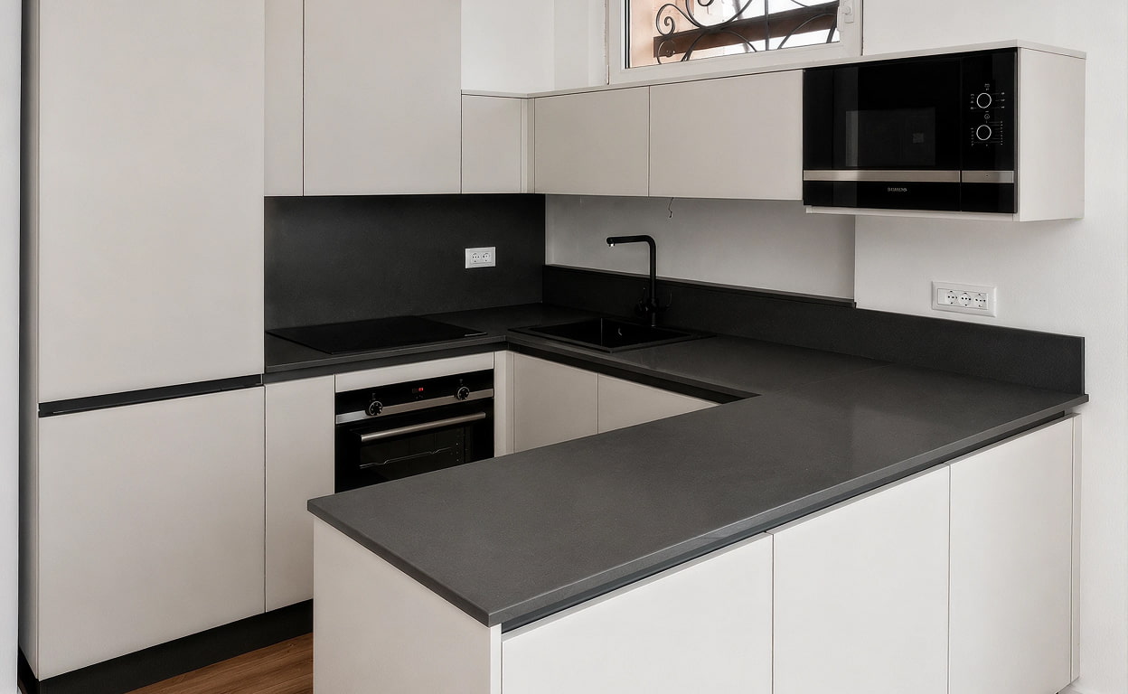 Cucina moderna con piano in pietra scura, lavello integrato e cucina con microonde da incasso, finiture bianche eleganti e luci pulite