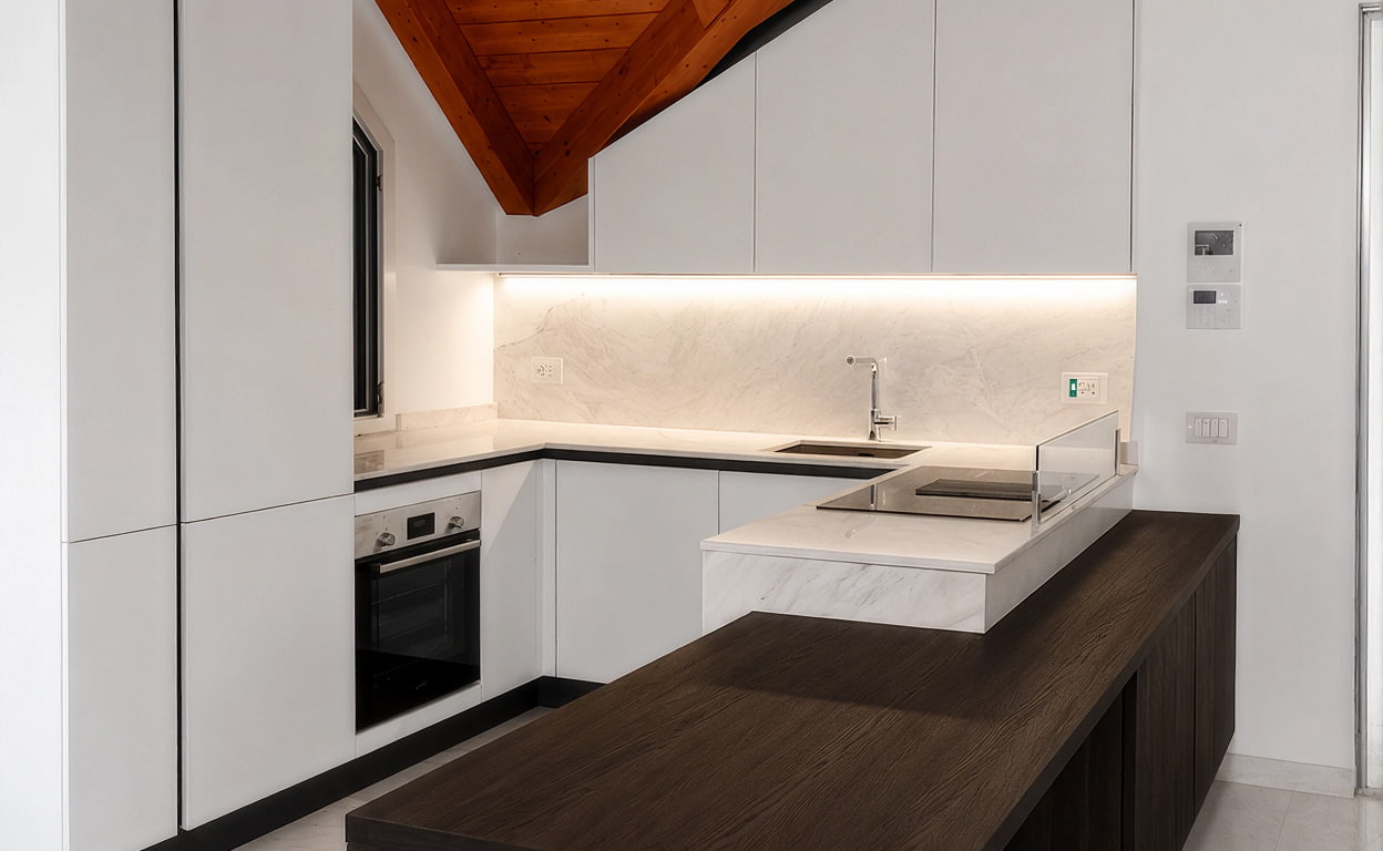 Cucina moderna bianca con top in quarzo chiaro, piano di lavoro scuro e finiture minimal, con illuminazione LED sotto pensili e lavello con rubinetto.