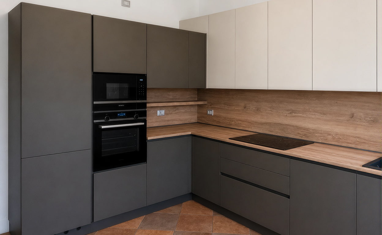 Cucina moderna ad angolo con ante grigie opache, piani in legno chiaro e elettrodomestici integrati, ambiente luminoso e minimal