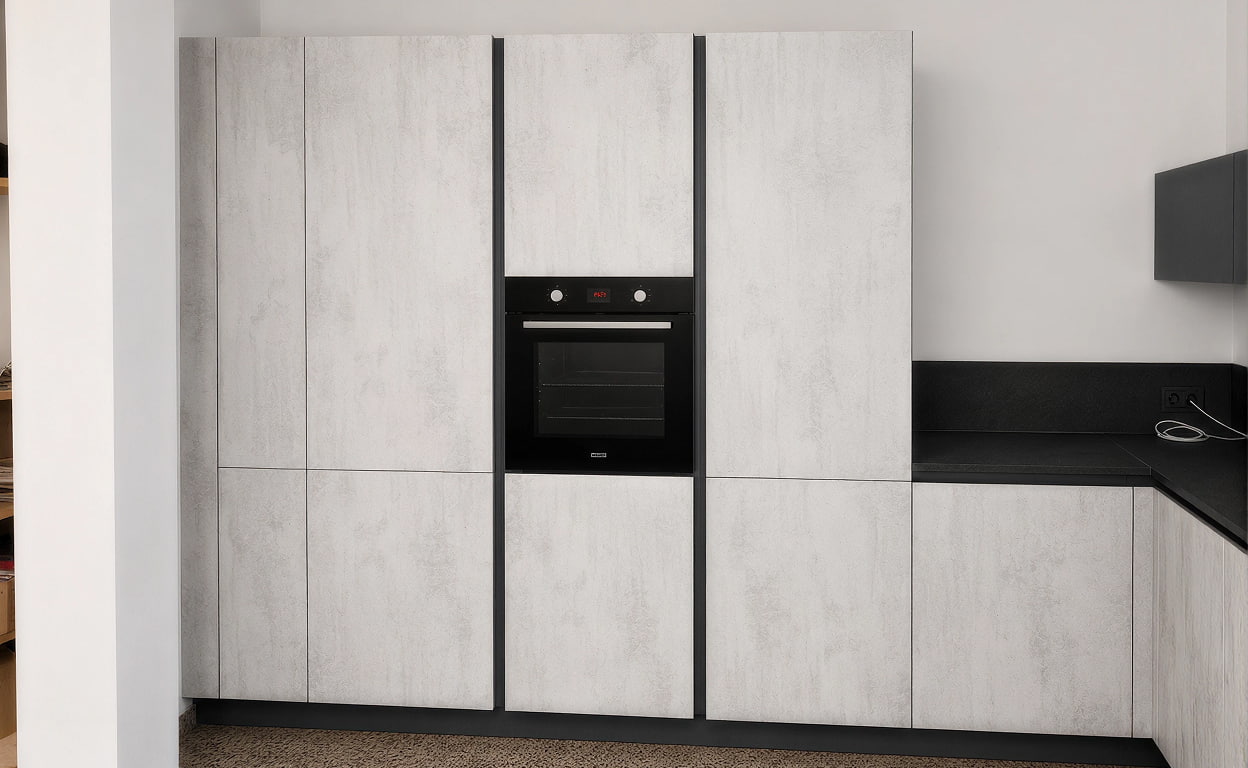 Cucina moderna con ante in finitura grigio chiaro e una colonna con forno da incasso nero, dettagli minimal e parete in stile contemporaneo, ambiente luminoso.