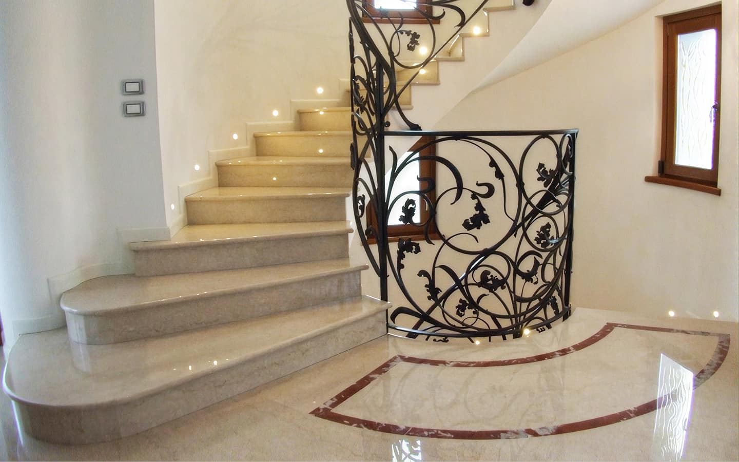 Interno di una casa elegante con scala in marmo chiara, ringhiera in ferro battuto decorata e pavimento lucido, illuminazione a soffitto e porta finestra