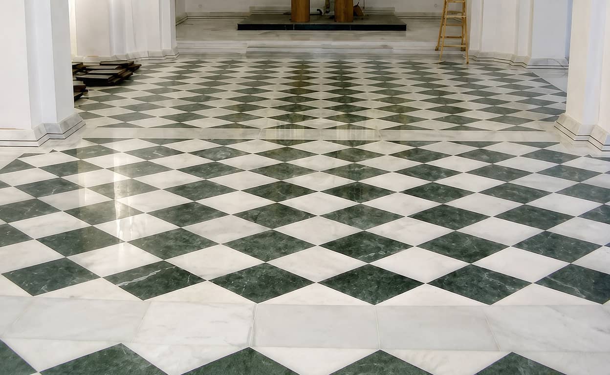 Pavimento in piastrelle esagonali e geometriche bianche e verdi, motivo a rombi su vasta area, in un interno luminoso con scala in metallo e dettagli decorativi