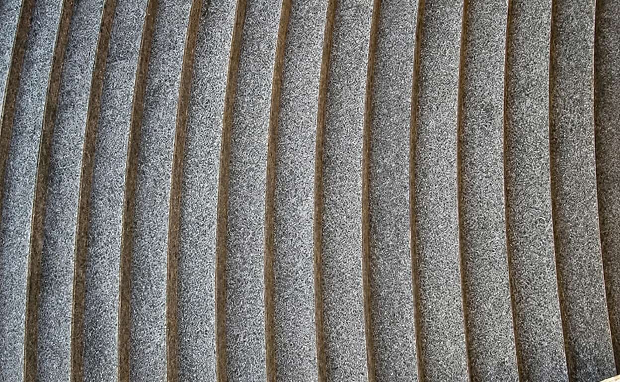 Primo piano di una superficie con righe sottili verticali in metallo e texture grigio argento, con inserti marroni tra le bande, dettaglio di pattern industriale.