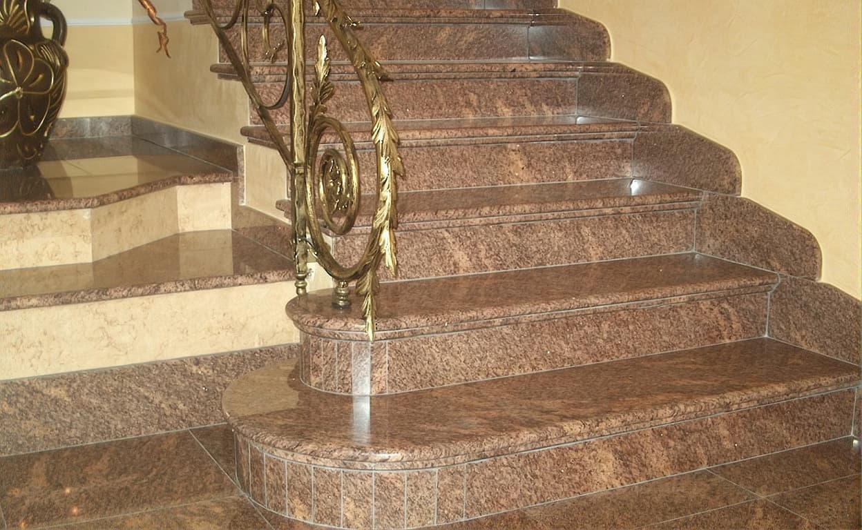 Scale in marmo con gradini lucidi e corrimano decorato in ottone, con elementi ornamentali e luci calde in un interno elegante.