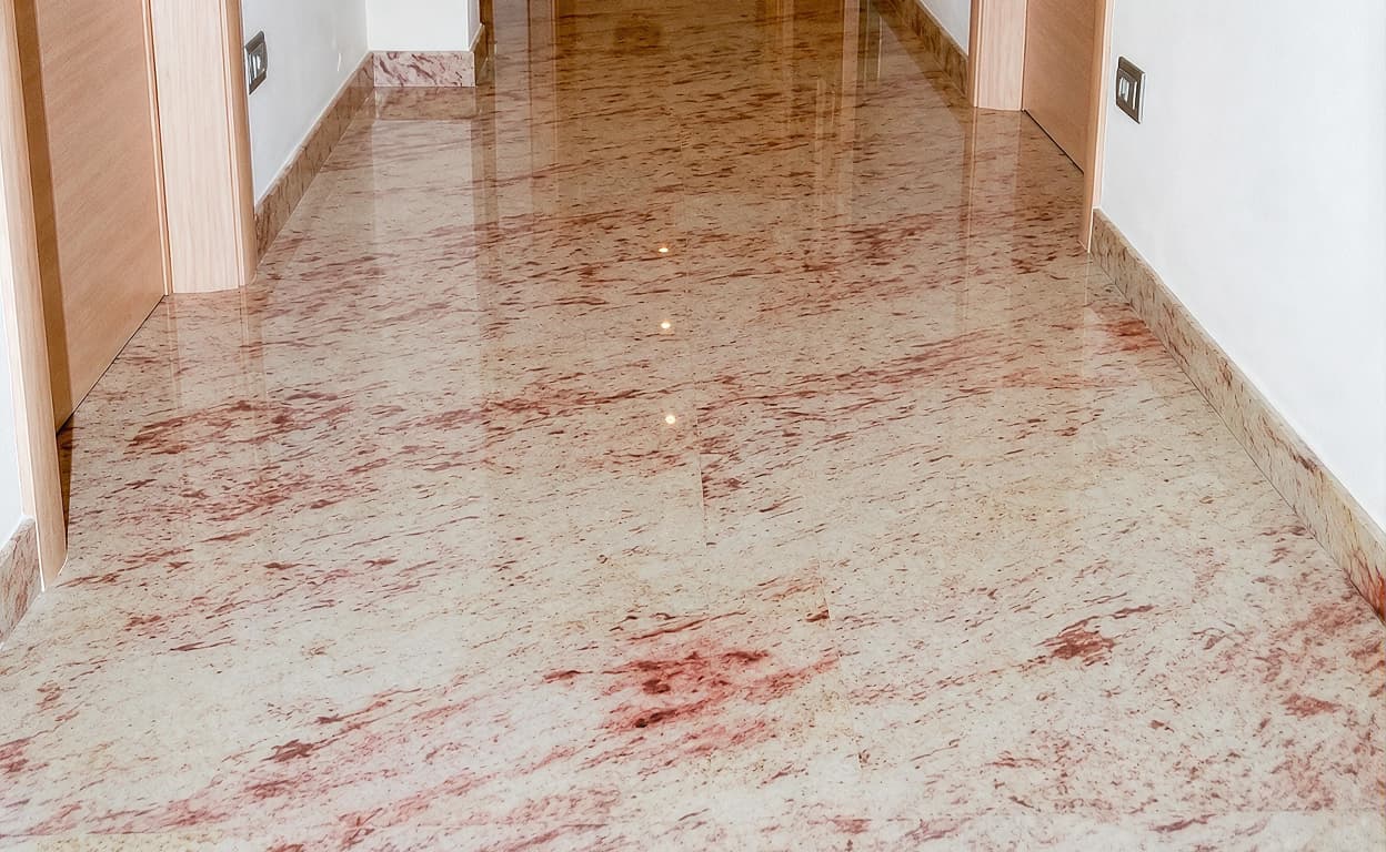 Pavimento in marmo chiaro e venature rosse lucide in un corridoio, pareti bianche e dettaglio di una porta sullo sfondo, ambiente luminoso e moderno