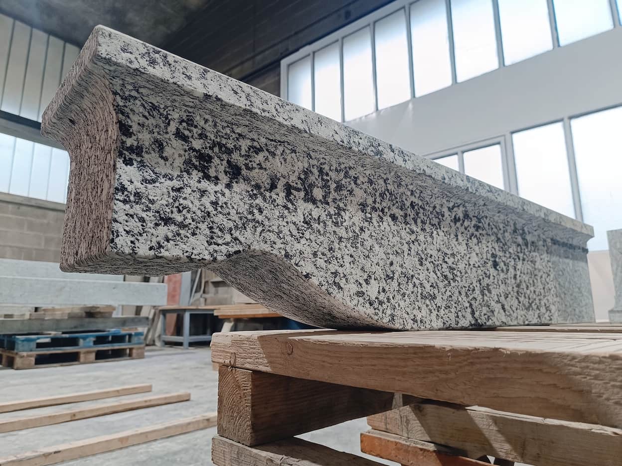Blocco di pietra naturale grigia levigata in lavorazione in officina, con grandi lastre su pallet e luce naturale da finestre alte, struttura grezza