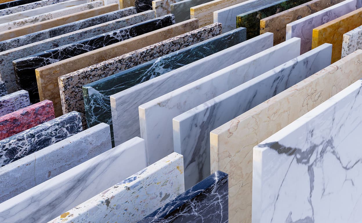 Lastre di marmo e pietra naturale in esposizione, con venature e finiture diverse, in un deposito o showroom di materiali edili.